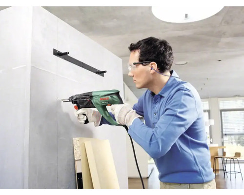 Un homme perce un mur avec une perceuse pour fixer un support d''étagère.