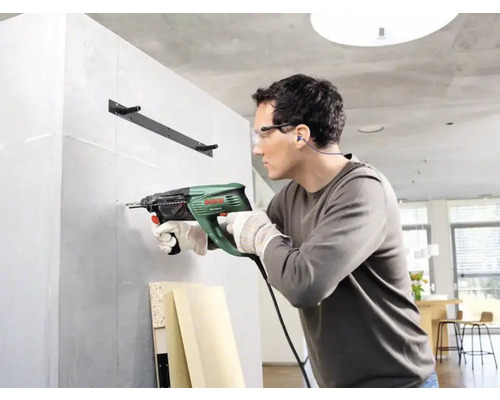 Un homme perce un trou dans un mur avec une perceuse à percussion.