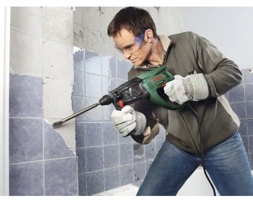 Un homme enlève du carrelage avec un marteau perforateur dans une salle de bain.