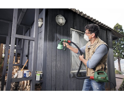 Mann streicht ein Holzhaus mit einem Farbsprühsystem