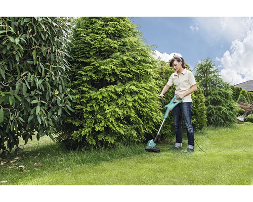 Frau benutzt Rasentrimmer im Garten.