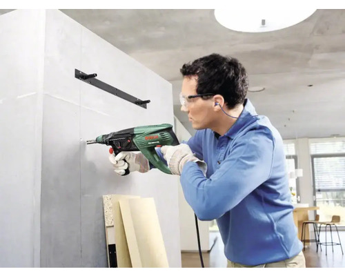 Un homme perce un trou dans un mur avec une perceuse.