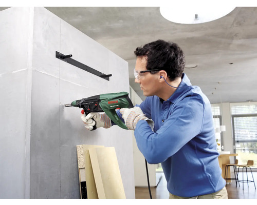 Un homme perce un mur avec une perceuse à percussion pour fixer un support