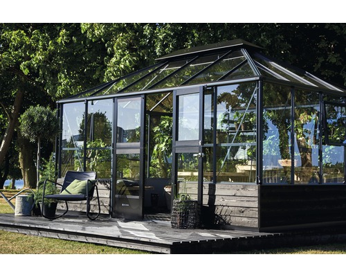 Serre avec parois en verre et cadre sombre sur terrasse en bois dans le jardin