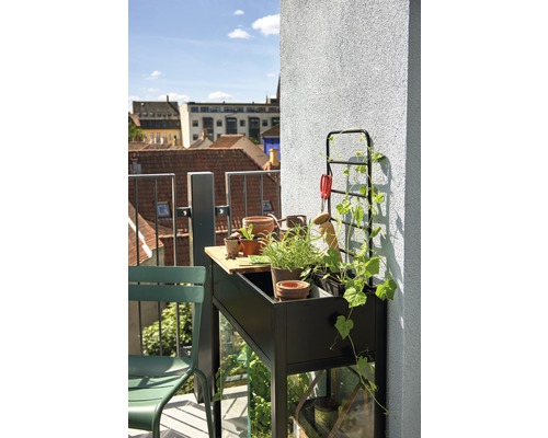 Balkonszene mit Hochbeet, Bepflanzung und Gartengeräten auf einem sonnigen Balkon