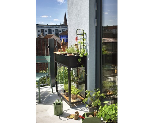 Balkonszene mit mobilem Hochbeet, Kräutern und Gartenzubehör.