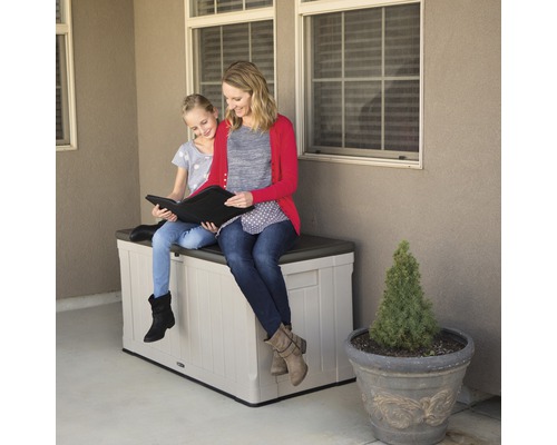 Eine Frau und ein Mädchen sitzen auf einer Aufbewahrungsbox im Freien und schauen sich ein Buch an.