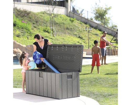 Szene im Garten mit einer grauen Gartenbox, in der Familienmitglieder Poolutensilien verstauen