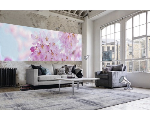 Wohnzimmer mit Sofa, Sessel, Tisch, Teppich und Wandbild mit Blütenmotiv in einem hellen Raum.