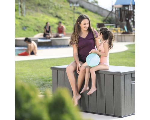 Zwei Mädchen sitzen auf einer grauen Gartenbox in einem Garten