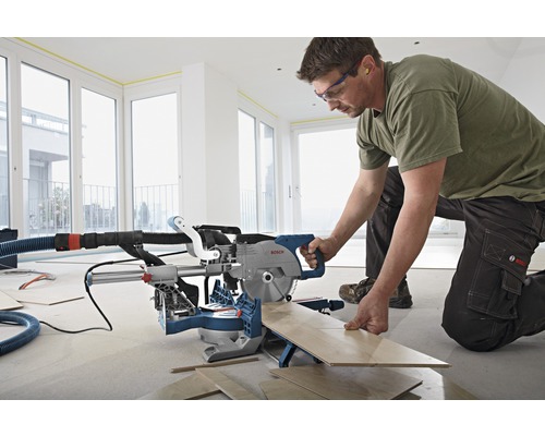 Un homme utilise une scie à onglet pour couper du bois dans une pièce lumineuse.
