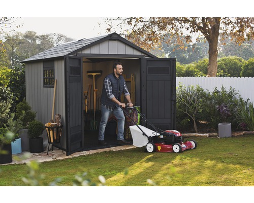 Un homme sort une tondeuse à gazon d''une remise de jardin dans un jardin.