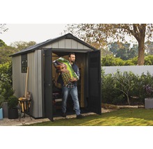 Un homme transporte du terreau hors d''un cabanon de jardin gris avec portes ouvertes