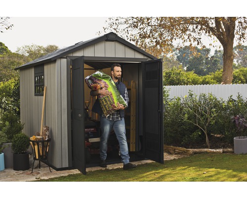 Un homme transporte du terreau hors d''un cabanon de jardin gris avec portes ouvertes