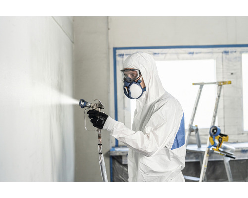 Mann mit Schutzanzug, Schutzbrille und Maske beim Sprühen einer Wand mit einer Farbspritzpistole