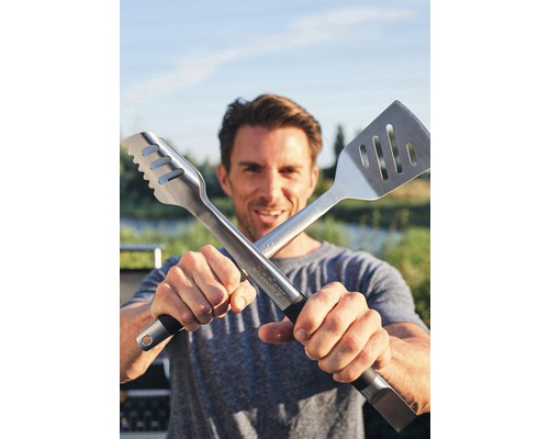 Mann hält Grillzange und Grillwender gekreuzt in die Kamera.