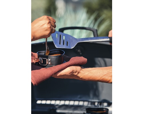 Szene mit Essen im Topf, Grillbesteck und Handtüchern vor einem Grill