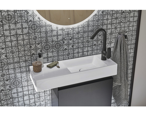 Badezimmerwaschtisch mit Armatur, Handtuch und Spiegel vor gemusterter Wand