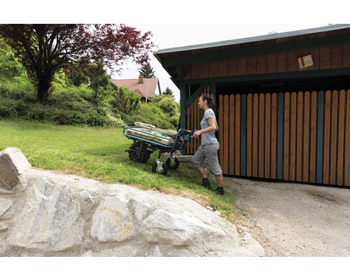 Frau schiebt eine Sackkarre mit Säcken durch den Garten.