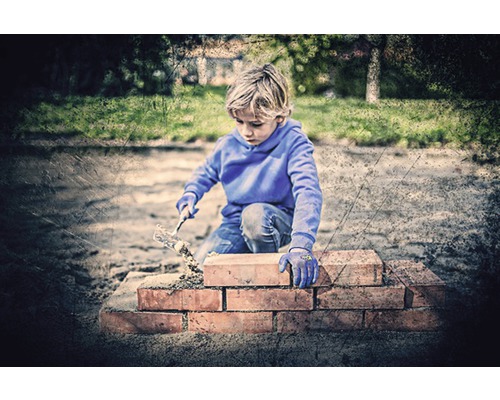 Junge baut eine Mauer mit Steinen und einer Maurerkelle