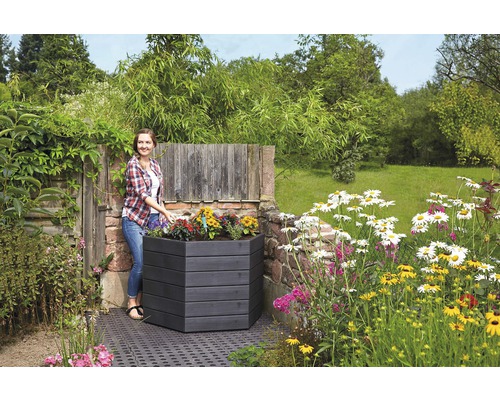 Une femme plante un potager surélevé hexagonal en bois dans le jardin.