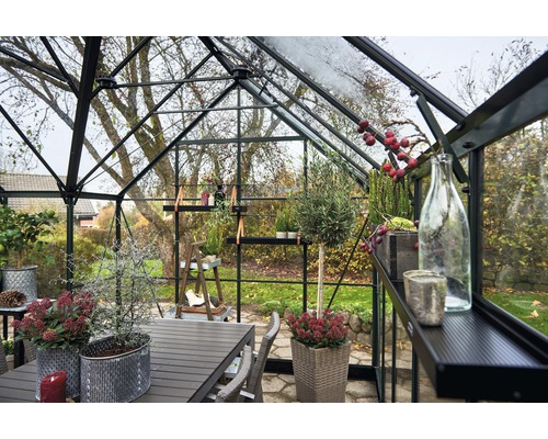 Gewächshaus mit Pflanzen, Tisch und Stühlen im Innenraum, helle und organisierte Atmosphäre