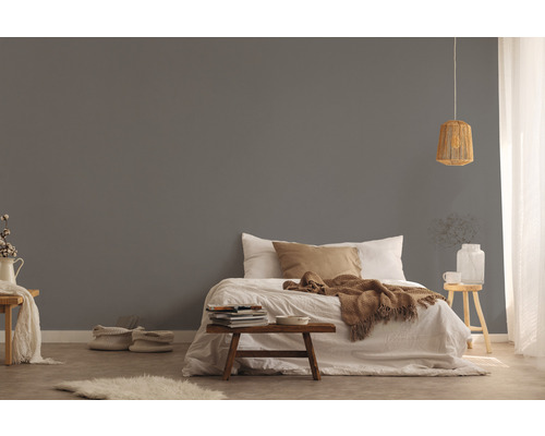 Einrichtung eines Schlafzimmers mit Bett, Nachttisch und dekorativen Elementen vor einer grauen Wand.