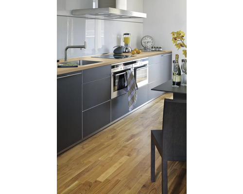 Cuisine claire avec kitchenette, évier, cuisinière, hotte aspirante, deux fours et table à manger avec chaise sur parquet.
