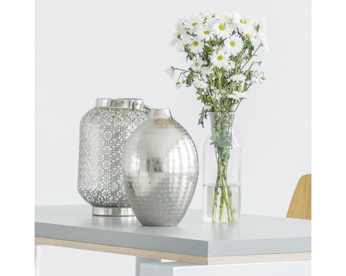 Scène décorative avec photophore, vase et bouquet sur une table.