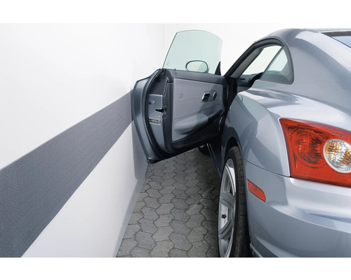 Graues Auto mit offener Tür und einem grauen Wandstoßschutz in einer Garage.