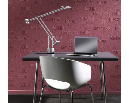 Bureau avec lampe, chaise et ordinateur portable devant un papier peint avec des noms de villes