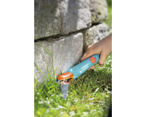 Cisailles à gazon Gardena utilisées pour tailler les bordures de pelouse à côté d''un mur de pierre.