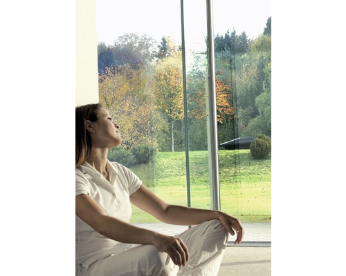 Femme assise devant une grande fenêtre donnant sur un jardin