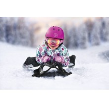 Kind mit Helm und Skibrille auf einem Schlitten im Schnee