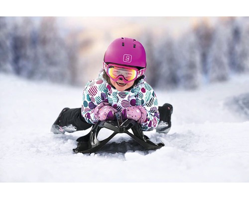 Enfant avec casque et lunettes de ski sur une luge dans la neige