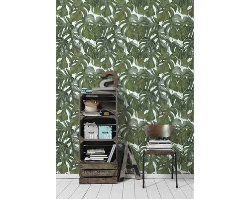 Wohnraum mit Monstera-Blättertapete, Holzkistenregal und Stuhl mit Bücherstapel