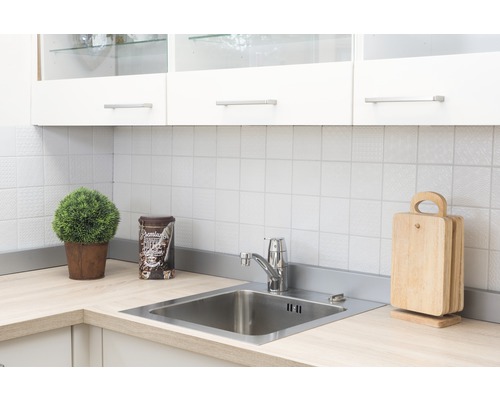 Küchenszene mit Spüle, Armatur, Schneidebrettern und Dekoration auf einer hellen Arbeitsplatte vor weißem Fliesenspiegel