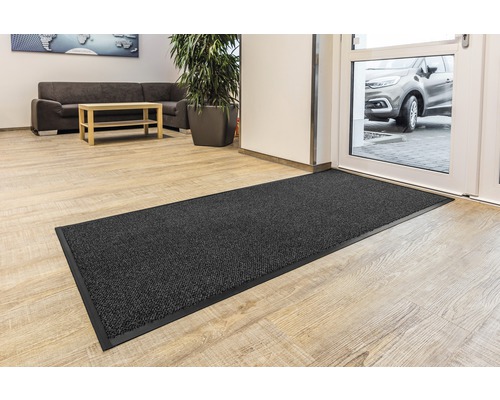 Paillasson noir avec bordure noire devant une porte d''entrée.