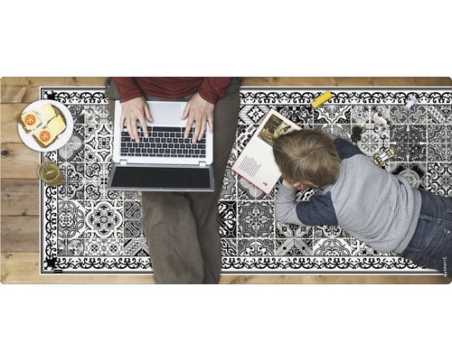 Dekorativer Teppich mit Fliesenmuster, darauf eine Person mit einem Laptop und ein Kind mit einem Buch liegend