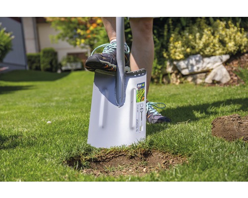 Une personne utilise une bêche dans le jardin pour faire un trou dans la pelouse.