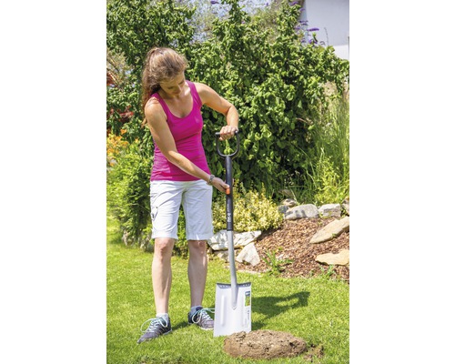 Une femme creuse un trou dans la pelouse du jardin à l''aide d''une bêche.