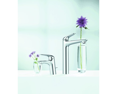 Deux robinets de lavabo en métal de différentes tailles avec des fleurs dans des verres.