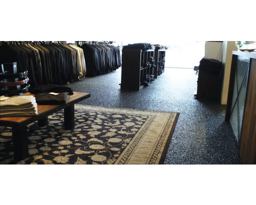 Innenansicht eines Bekleidungsgeschäfts mit Kleiderständern, Regalen und einem Teppich