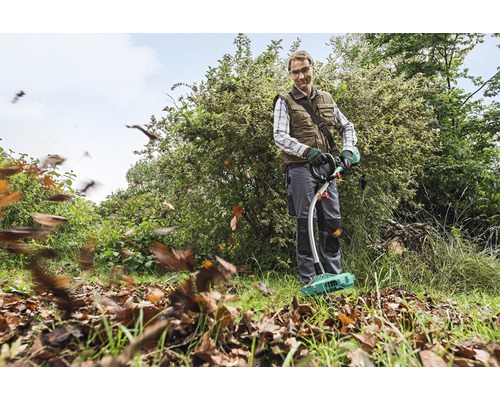 Ein Mann benutzt einen Laubsammler im Garten, um Blätter zu entfernen.
