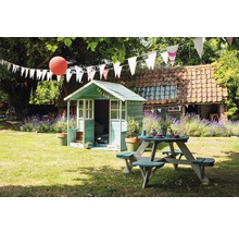 Scène de jardin avec cabane de jeu et table de pique-nique sous des guirlandes.