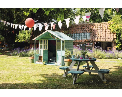 Scène de jardin avec cabane de jeu et table de pique-nique sous des guirlandes.