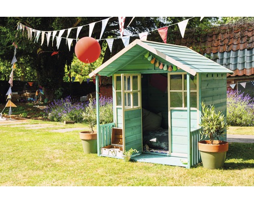 Une cabane de jeu verte dans un jardin avec décoration et plantes.