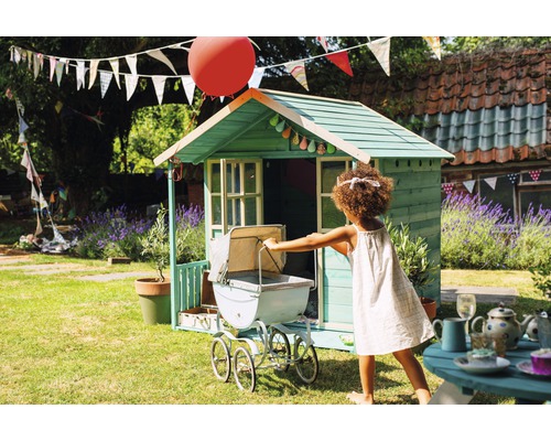 Enfant jouant avec une poussette devant une cabane de jeu dans le jardin.