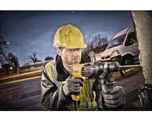 Un ouvrier du bâtiment portant un casque de protection perce un objet à l''extérieur avec une perceuse.