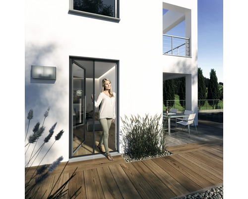 Moustiquaire Windhager PLUS store de porte sans perçage anthracite 160x225 cm Une femme ouvre une porte pliante dans une maison moderne avec une terrasse.